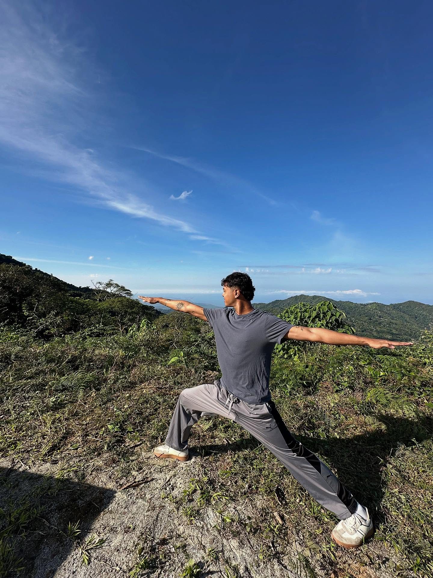Saranagatha Das en Virabhadrasana II sobre una loma de la Sierra Nevada, con el Caribe al fondo